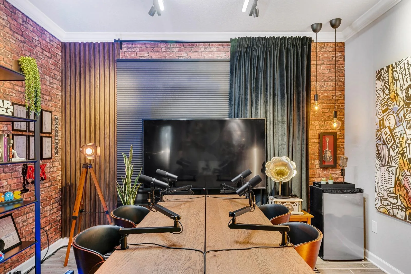 Podcast studio with four microphones, table, TV, brick and curtains
